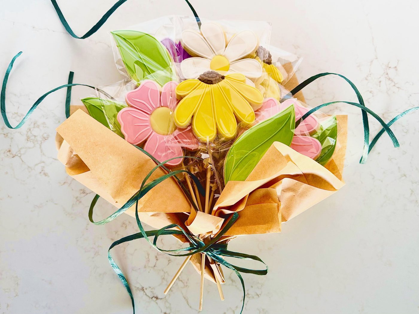 Cookie bouquet of decorated flower and leaf sugar cookies on sticks, wrapped in kraft paper with green ribbon