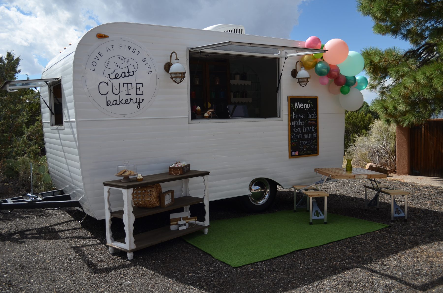 The Eat Cute Bakery vintage camper set up at an event with a dessert display table